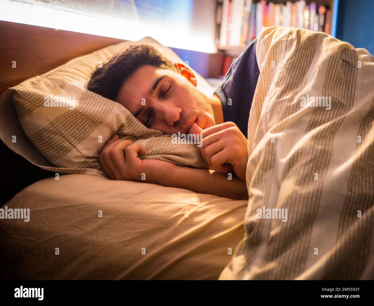 Young man sleeping on bed and sucking finger Stock Photo