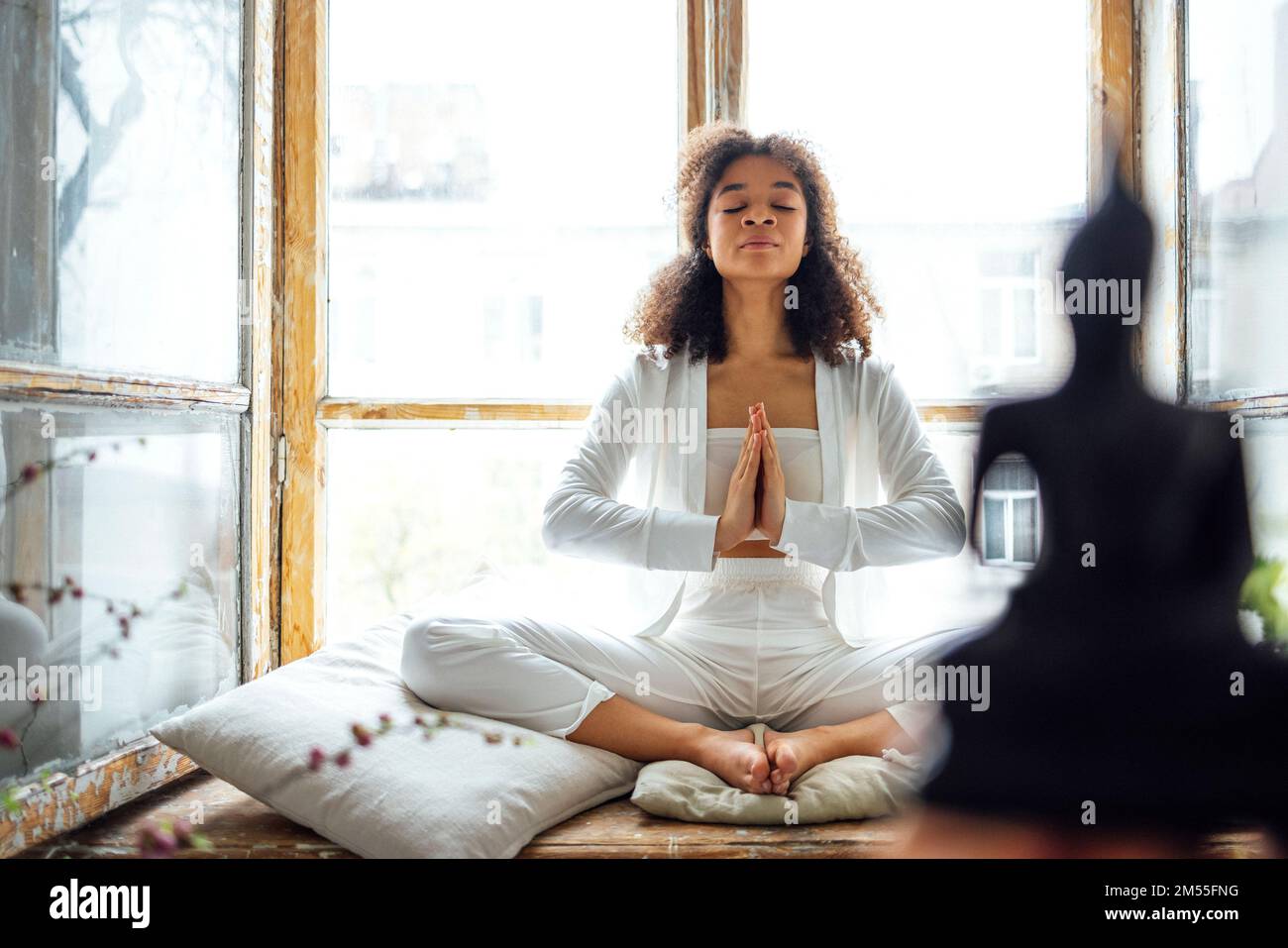 Young adult happy fit slim healthy African American ethnic woman wearing white clothes sitting in yoga pose at home in living room, doing fitness morn Stock Photo