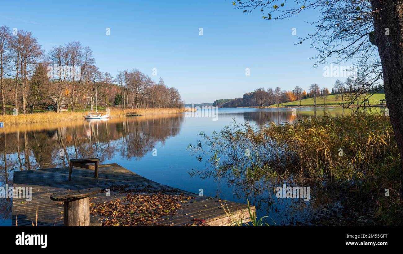 The boats by the coast with golden plants in a Lake Baltieji Lakajai with the reflection of trees in Moletai region in Lithuania Stock Photo