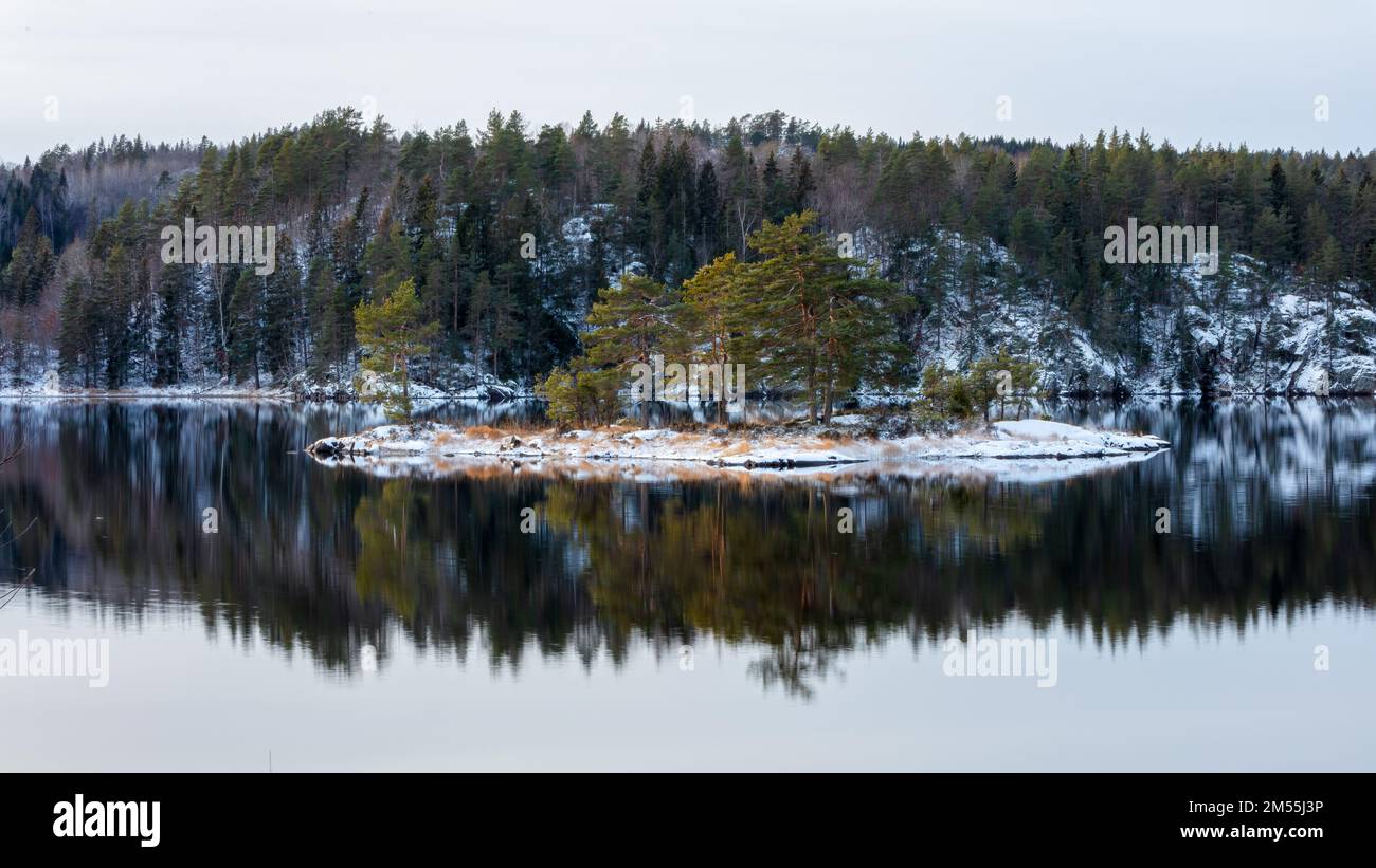 Winter landscape with forest and snow covered rocks, Beauiful reflection in the lake waters. Norway. Stock Photo