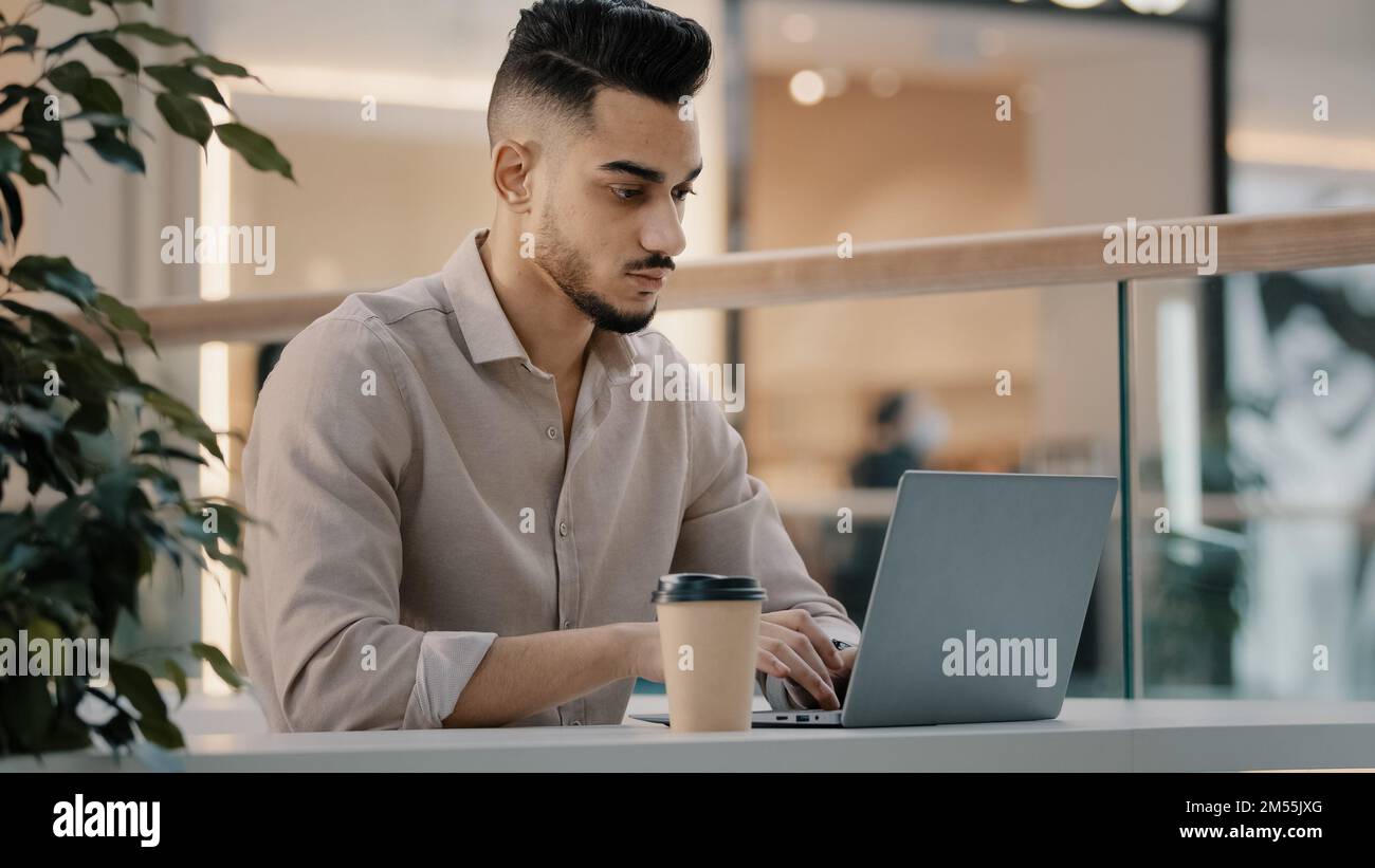 Indian Hispanic ethnic worker manager student businessman freelancer entrepreneur man guy typing business email sit at cafe table with laptop work Stock Photo