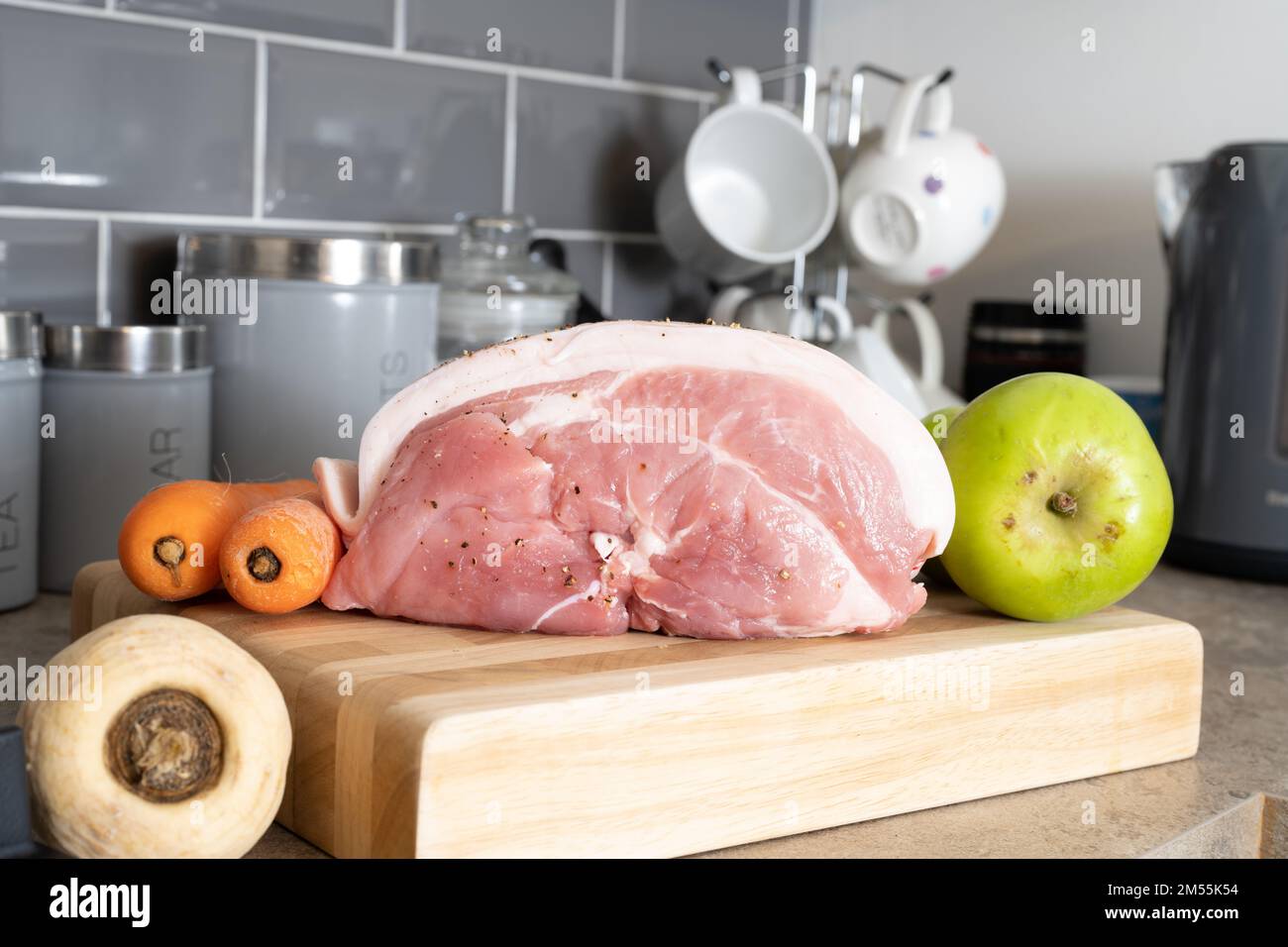 raw uncooked  Pork leg shoulder joint with cooking apple parsnip and carrots  on a wooden chopping board Stock Photo