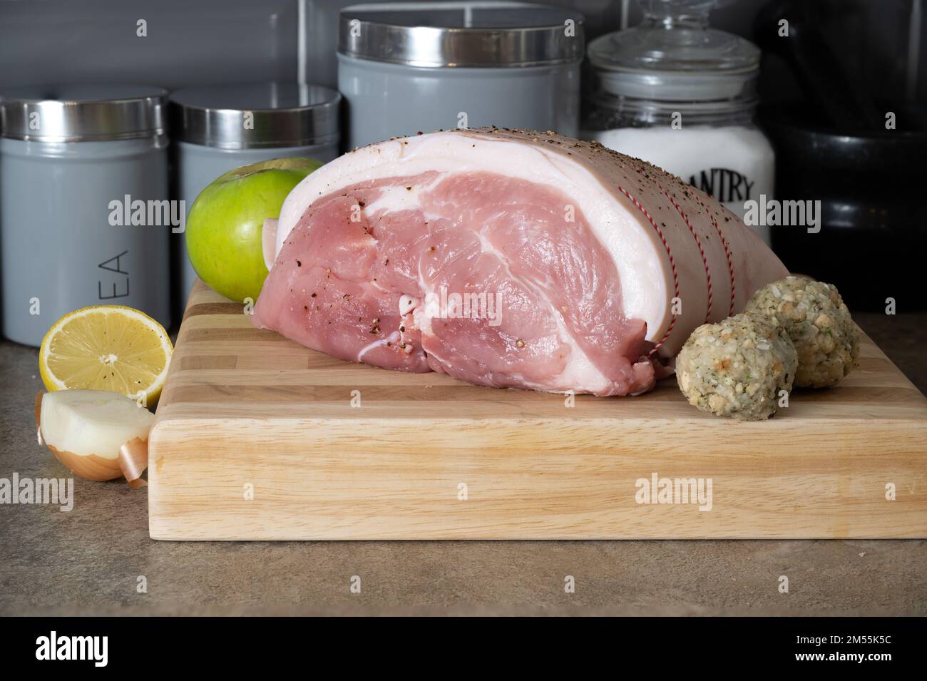 uncooked Leg of Pork joint on a beech block cutting board with onion, lemon  cooking apple and sage and onion stuffing balls Stock Photo