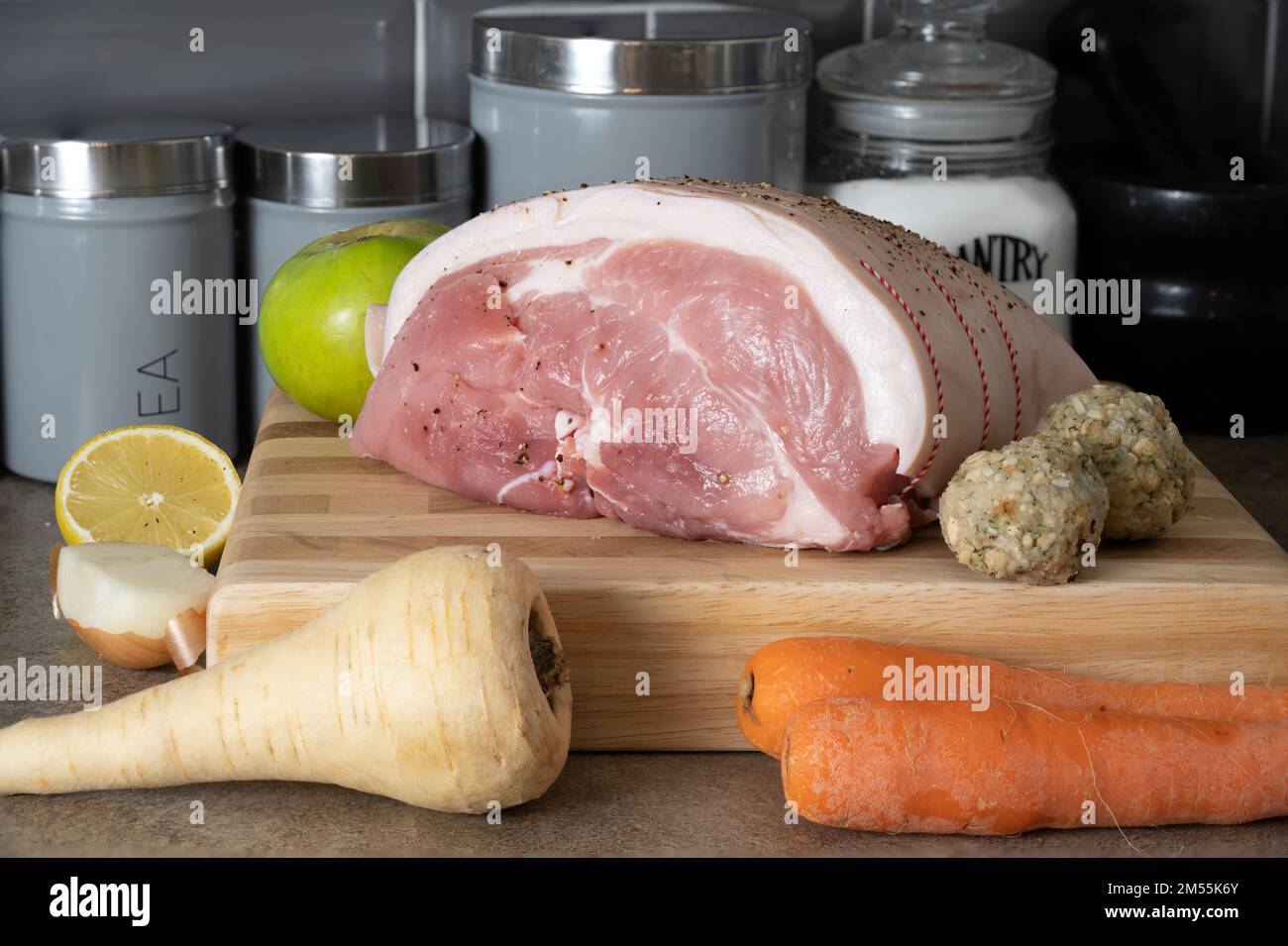 Raw uncooked Leg of Pork joint on a beech block cutting board with seasonable root vegetables cooking apple and sage and onion stuffing balls Stock Photo