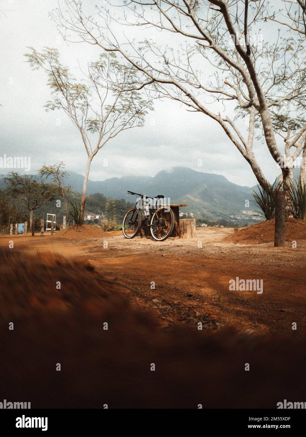 A vertical shot of a bicycle next to a wooden table with mountains in the background Stock Photo