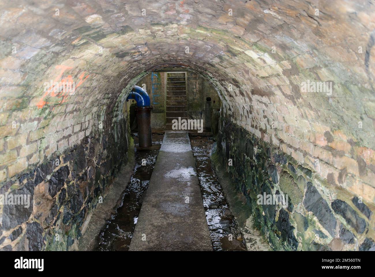 Dirty water runs down the sides of a path through a sewer tunnel Stock Photo