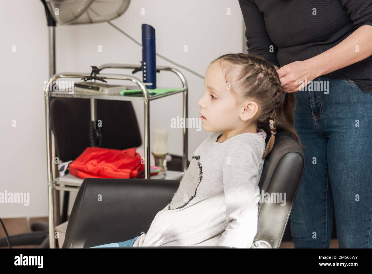 Hair salon, hairdresser makes hairdo braids for small girl in barber