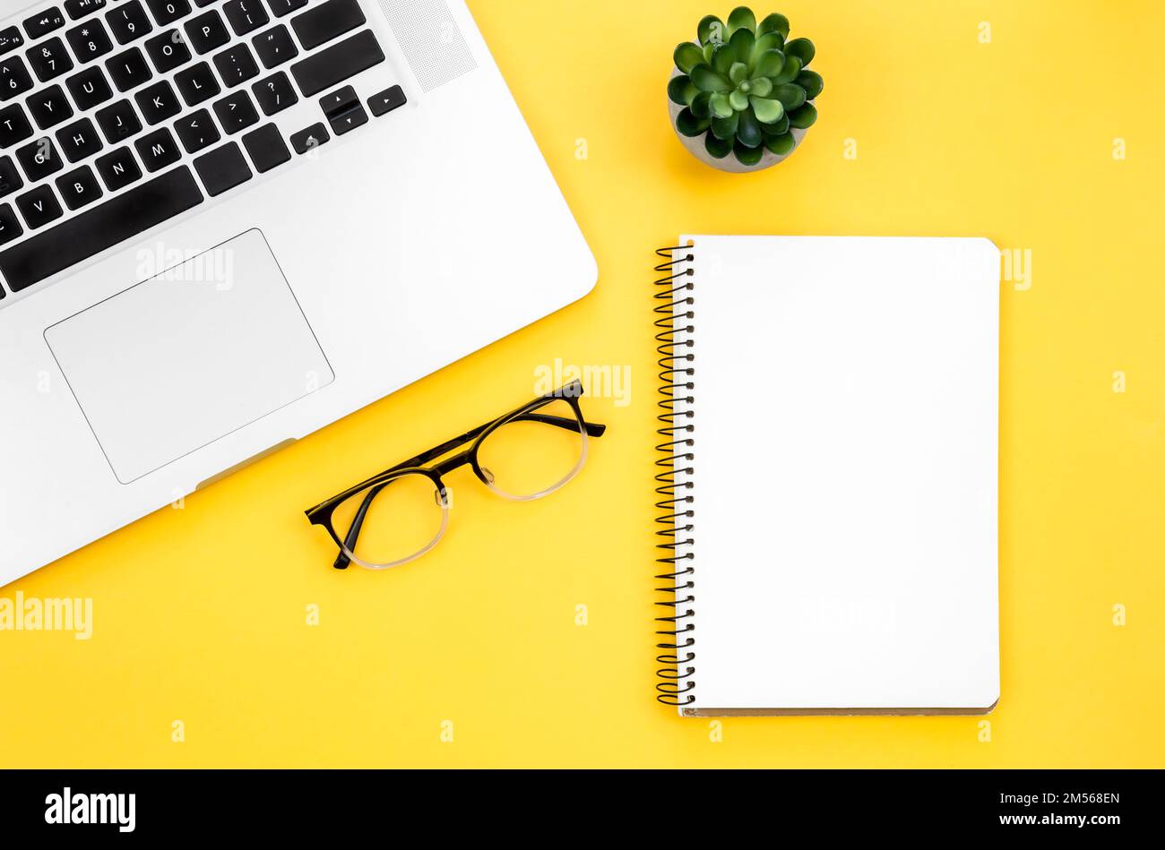 Laptop, glasses and blank notepad on yellow background, flat lay. Stock Photo