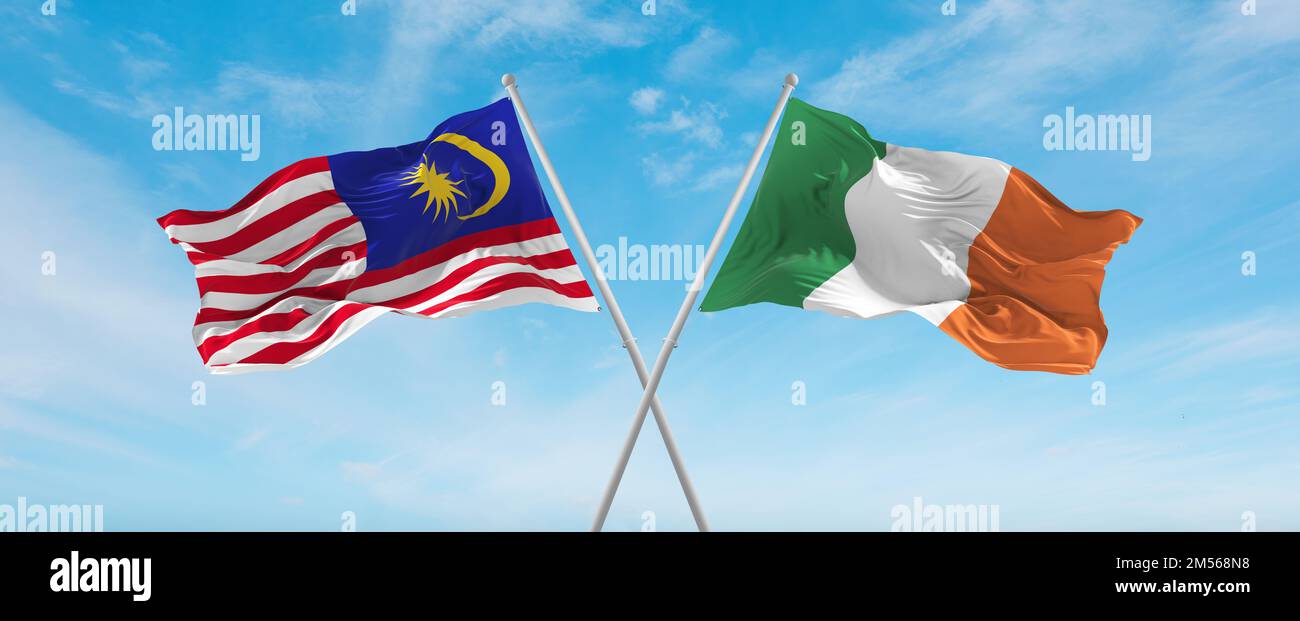 two crossed flags Ireland and Malaysia waving in wind at cloudy sky ...
