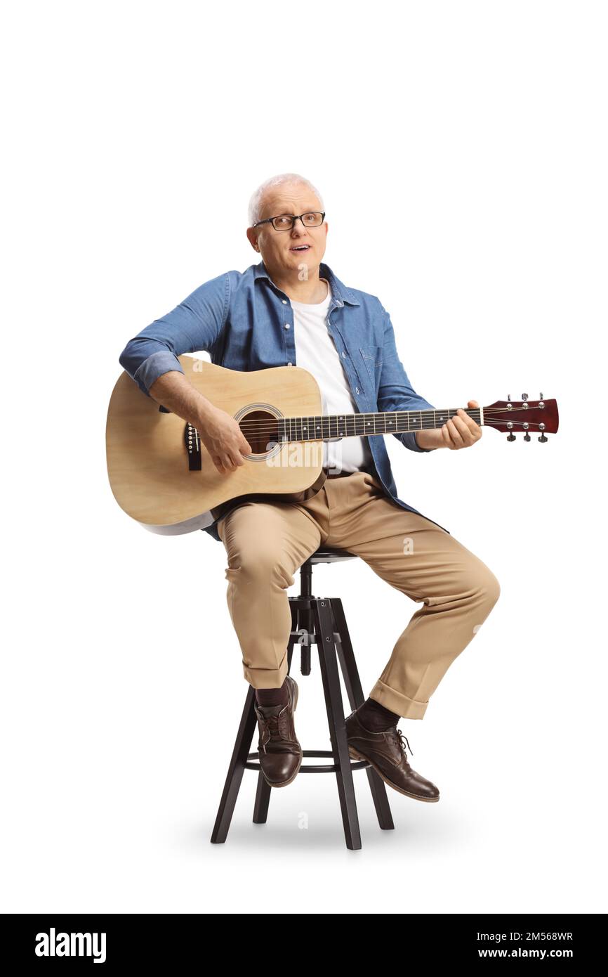 Mature man with an acoustic guitar sitting on a chair and singing ...