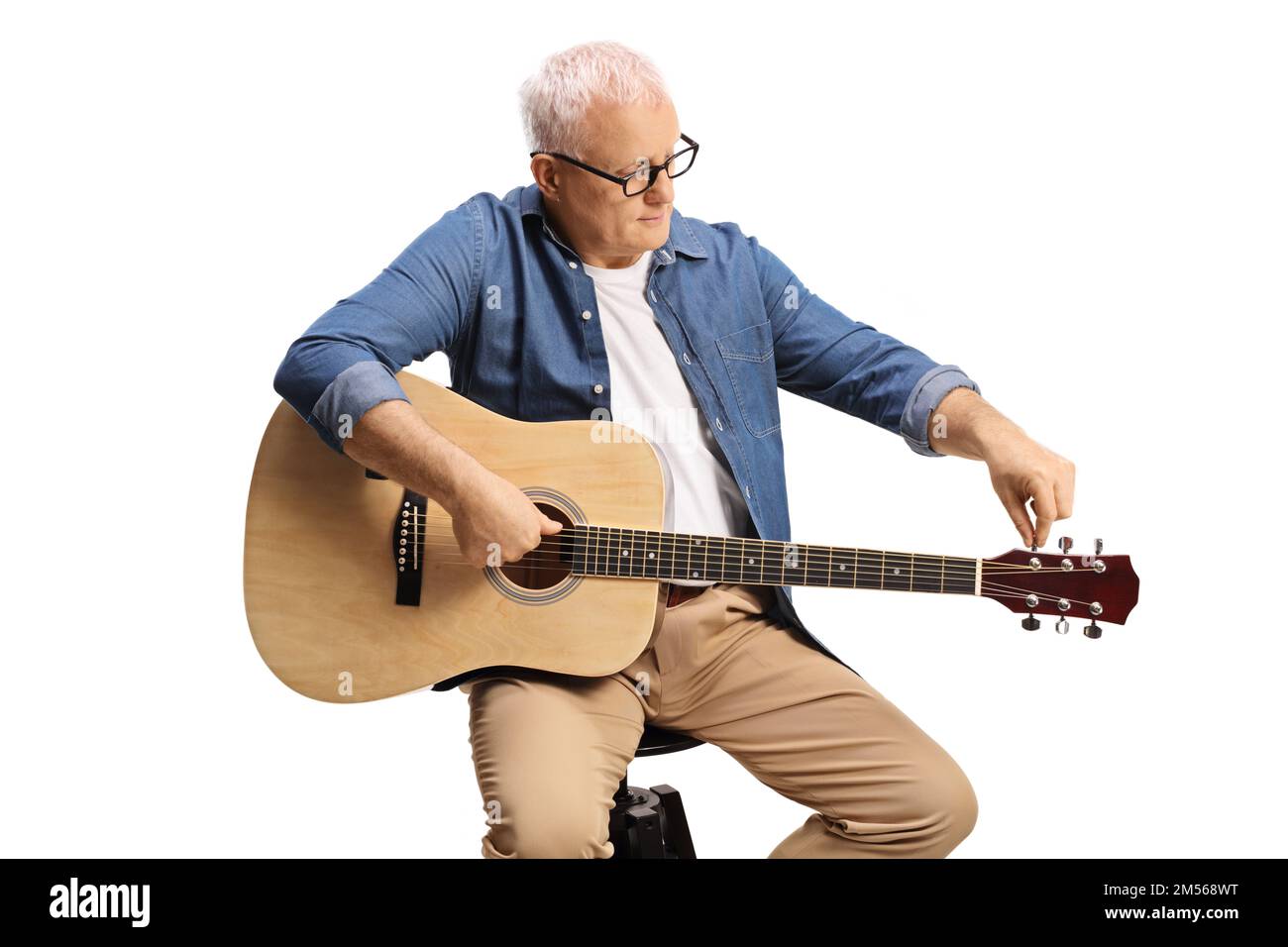 Mature man sitting on a chair and tunning an acoustic guitar isolated ...
