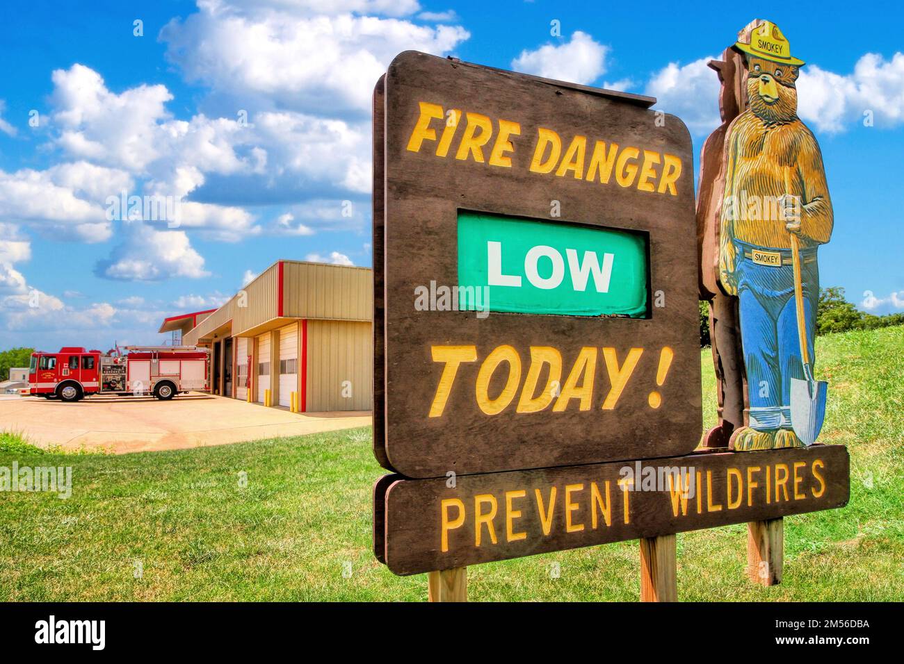 Chandler Oklahoma's Fire Department and EMS sits under a blue sky with white clouds with the Smokey Bear 'Fire Danger' wood sign in the foreground. Stock Photo