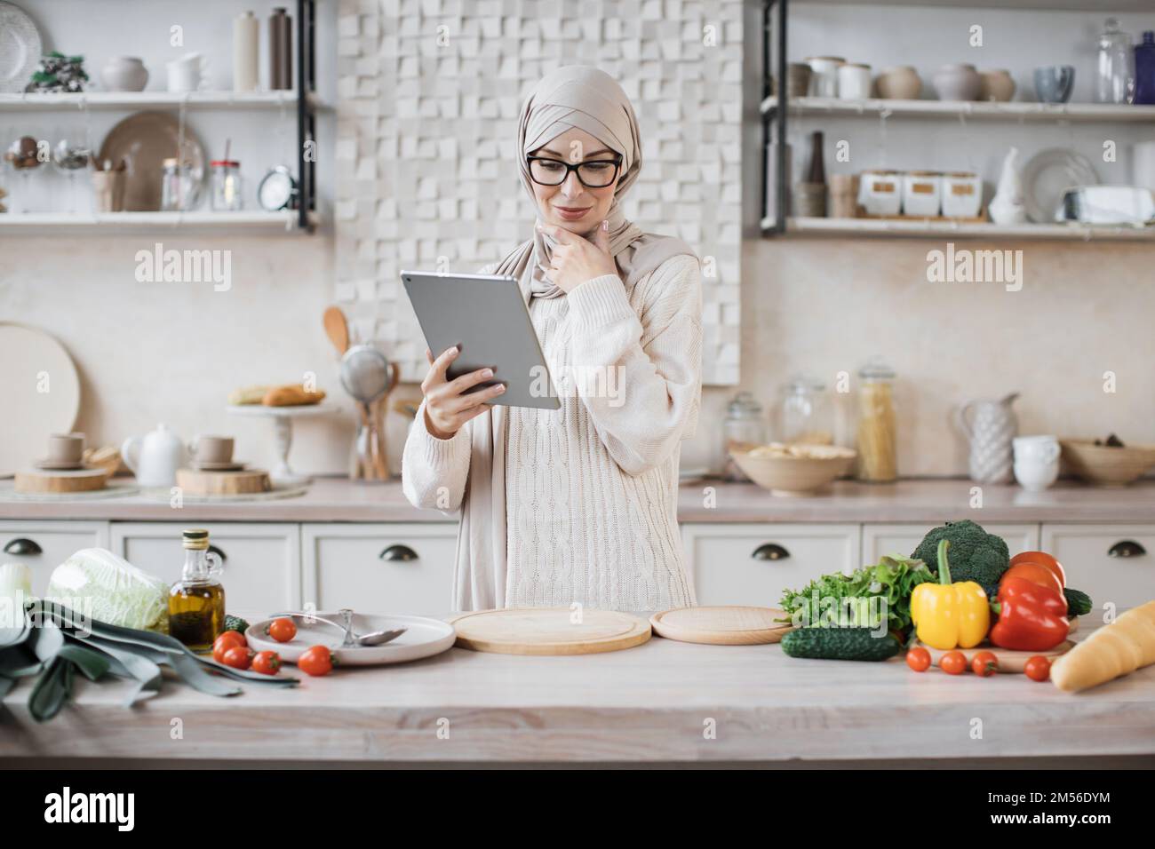 Cheerful young muslim woman in hijab cooking salad for dinner at home ...