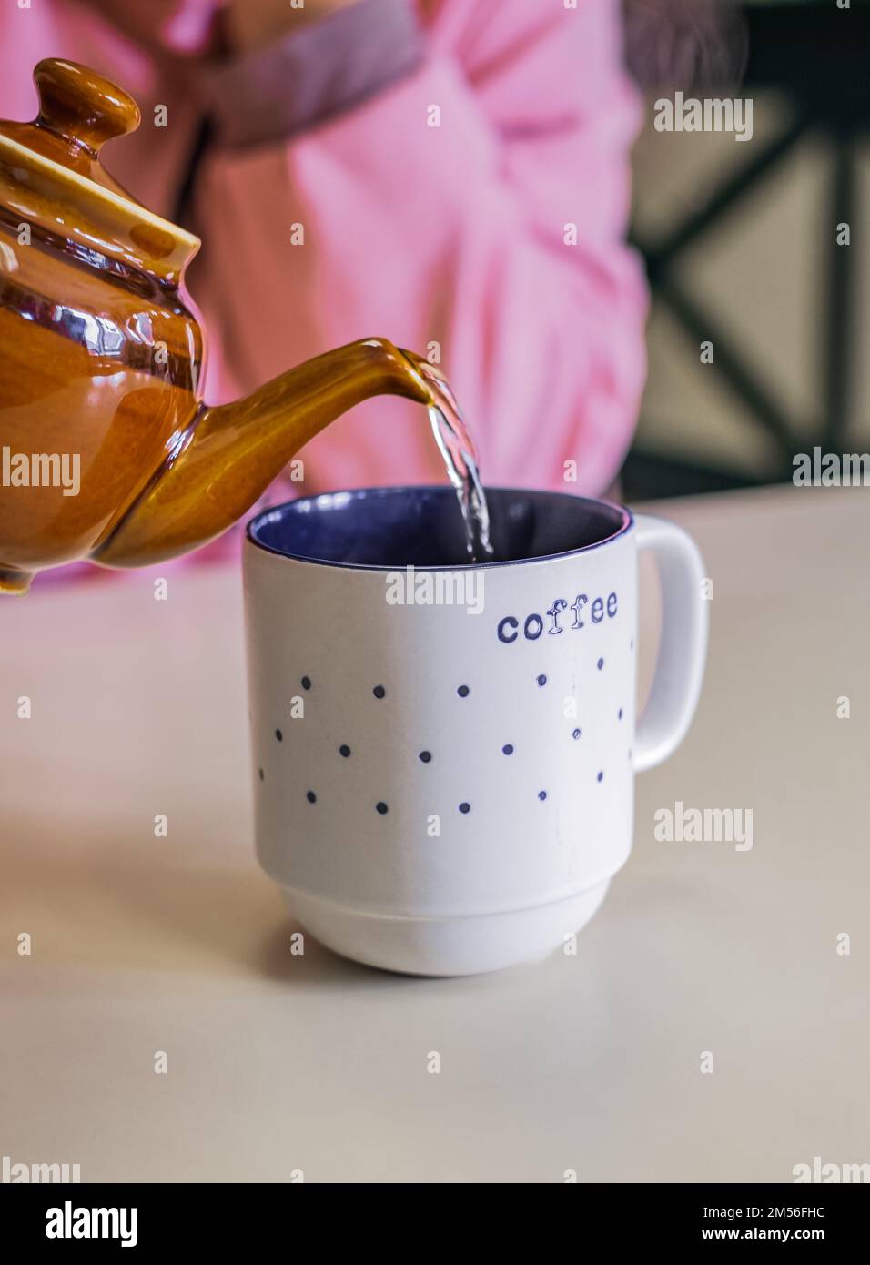 Hot tea in teapot and cup with steam on a table. Woman pour tea from brown teapot into a cup. The process of brewing tea, pouring hot water from the k Stock Photo