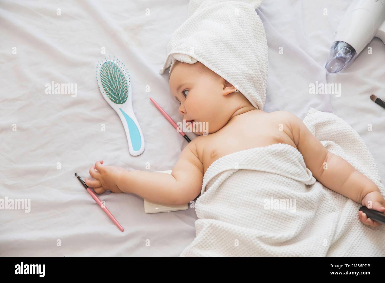 baby with towel on her head lies near the hairdryer,cosmetics and comb Stock Photo