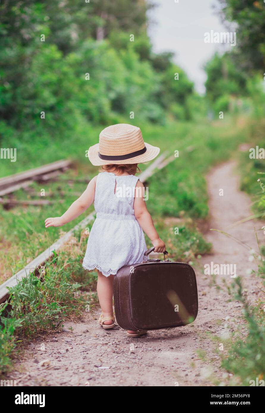 Charming baby with a suitcase walks along the railroad Stock Photo