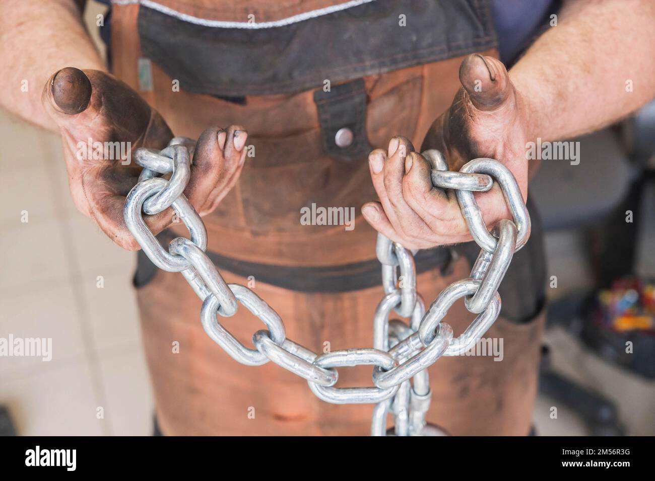 workshop worker in dirty brown clothes holds steel chain in hands  Stock Photo