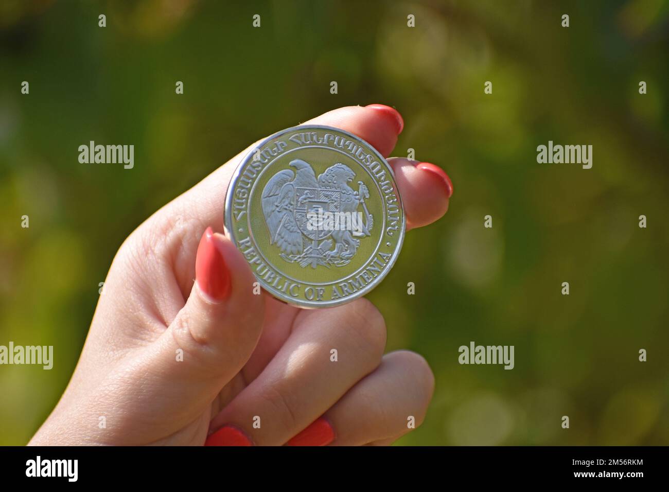 A close up of a woman's hand holding a coin with the Coat of arms of Armenia on it, blurred background Stock Photo