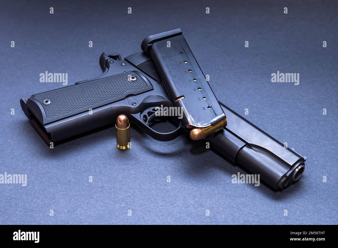 A 45 caliber 1911 model pistol with a loaded magazine on top of it and another bullet next to it with a dark background Stock Photo