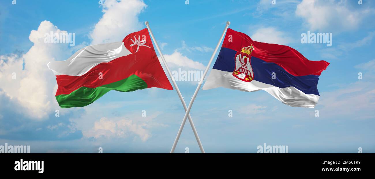 two crossed flags Serbia and Oman waving in wind at cloudy sky. Concept ...