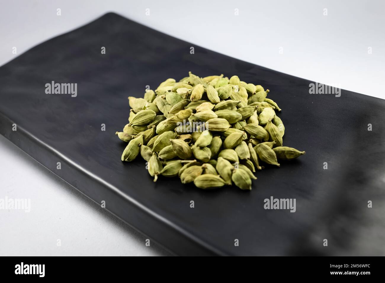 A closeup of green cardamom or green elaichi on black platter isolated on white background. Stock Photo