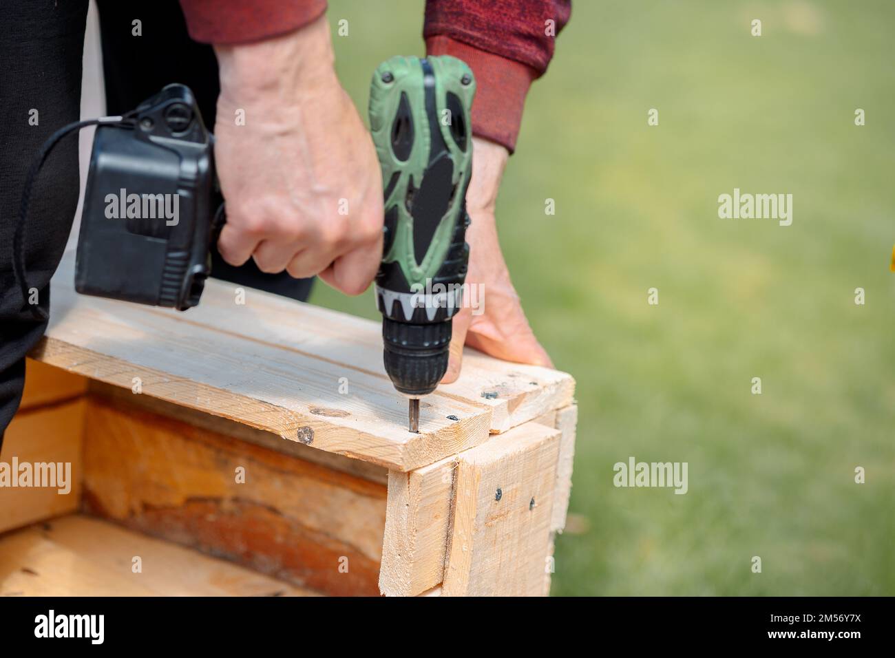 Man is screwing screw into wooden box with cordless screwdriver