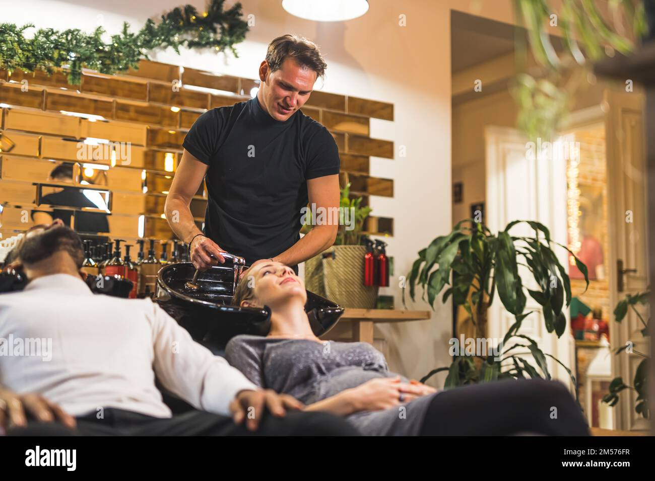 Two people sit on shampoo chairs in hairdresser salon. Pregnant woman having her blond hair washed by a professional hairstylist. High quality photo Stock Photo