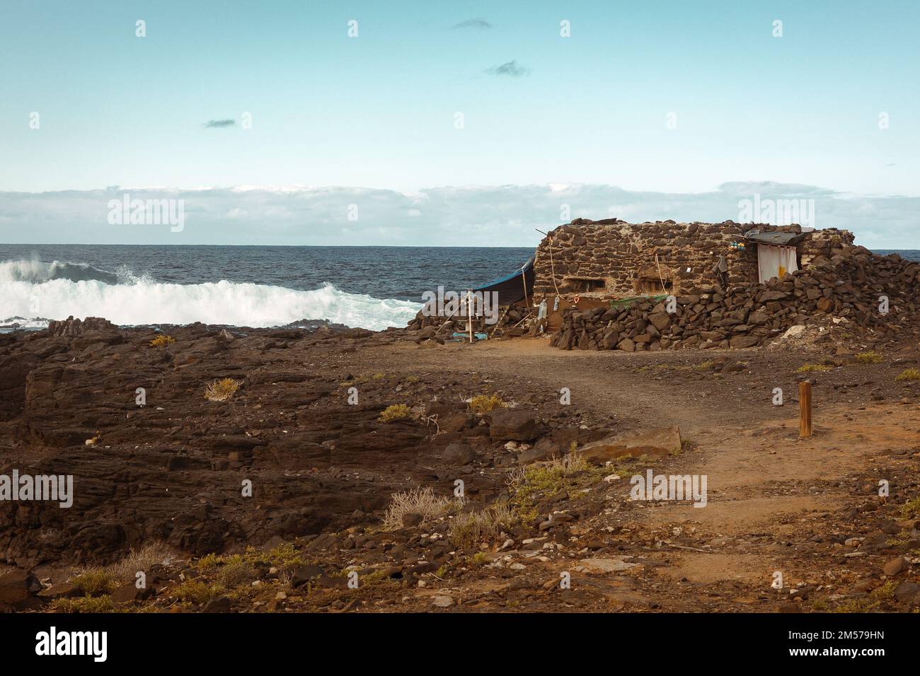 The remains of a stone building by the shoreline of a sea with foamy ...