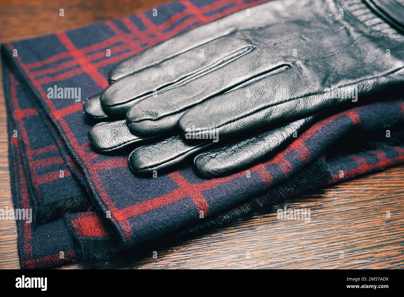 Men's leather gloves and a plaid scarf on a wooden table close-up Stock Photo