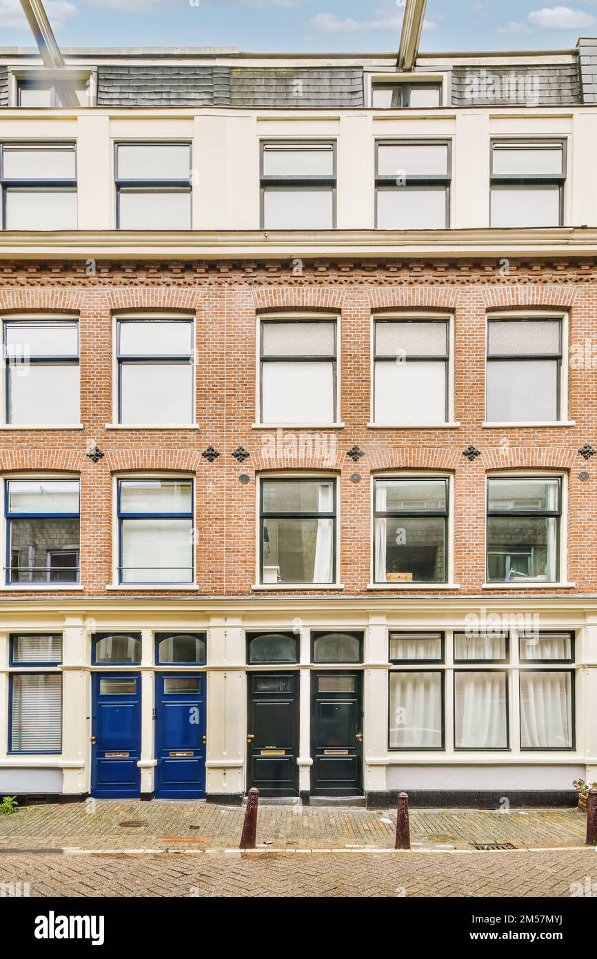 an old brick building in amsterdam, with blue doors on the front and windows open to let you into your home Stock Photo
