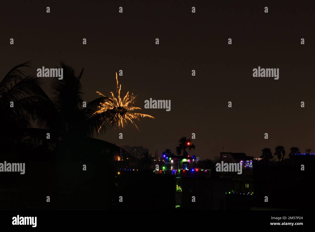 firework during celebration of new year, diwali and other festivals. shot taken against night sky with colorful lights in distant houses. Stock Photo