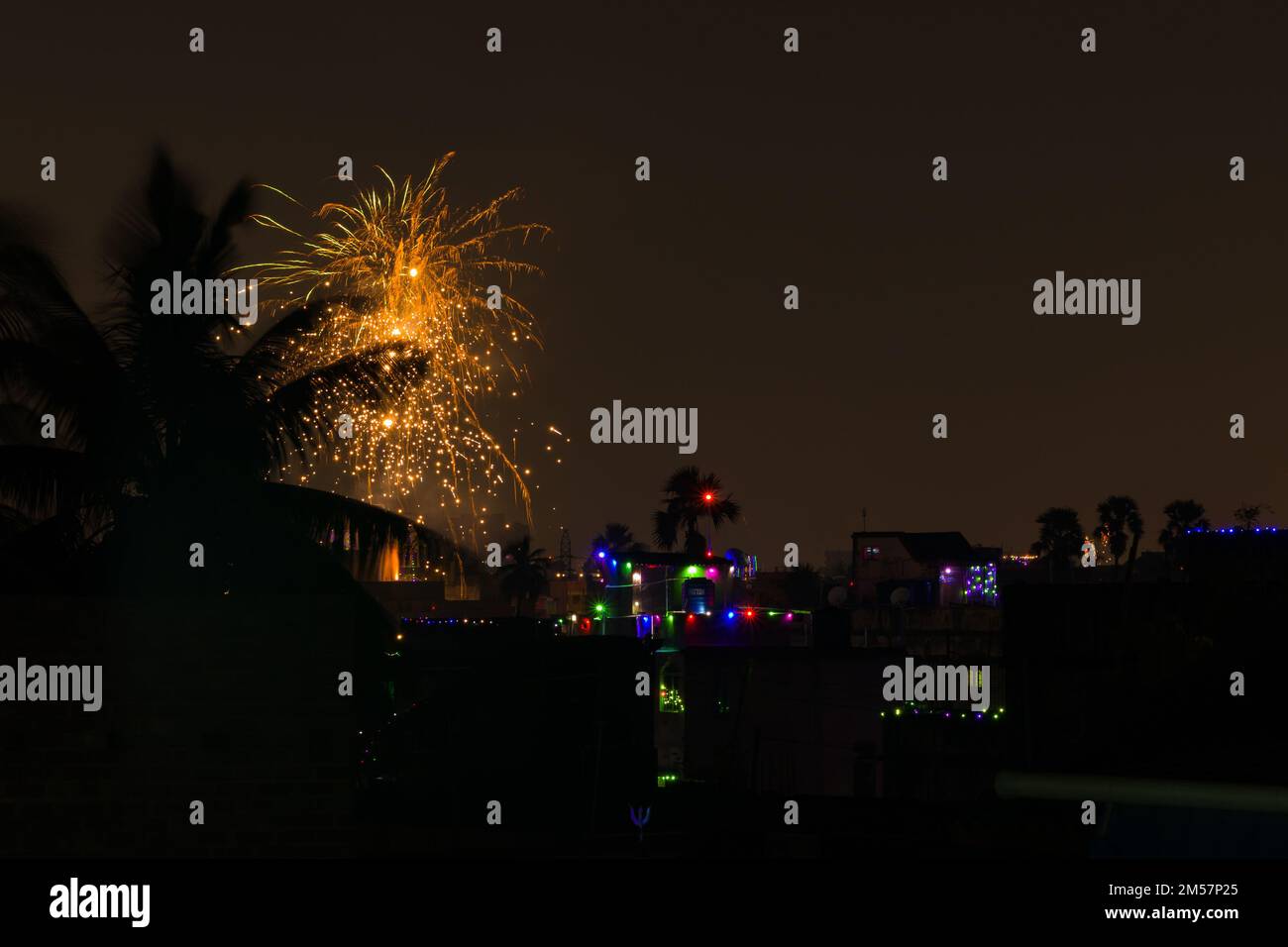 firework during celebration of new year, diwali and other festivals. shot taken against night sky with colorful lights in distant houses. Stock Photo