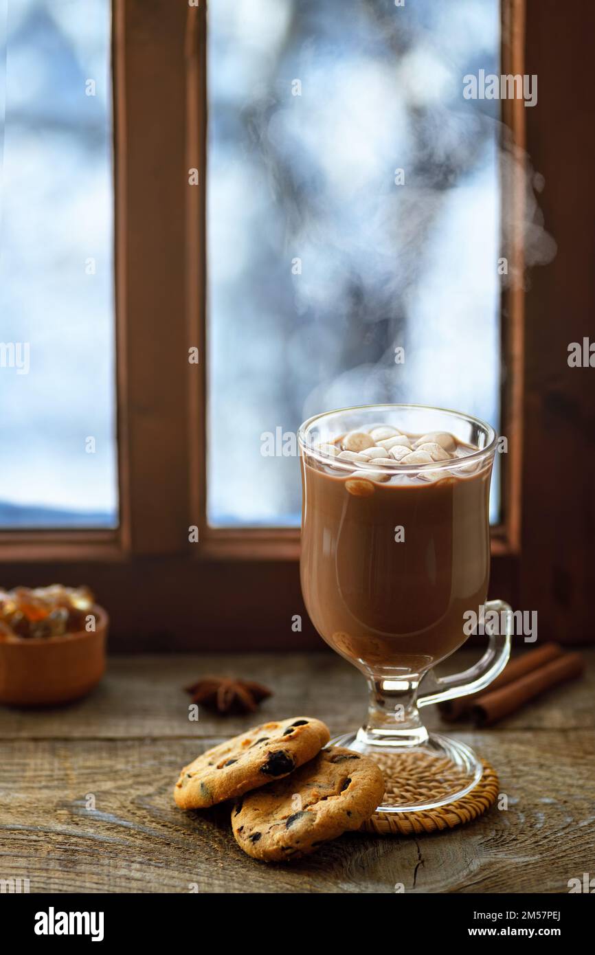 hot chocolate or cocoa with marshmallows in glass cup on table with winter window Stock Photo