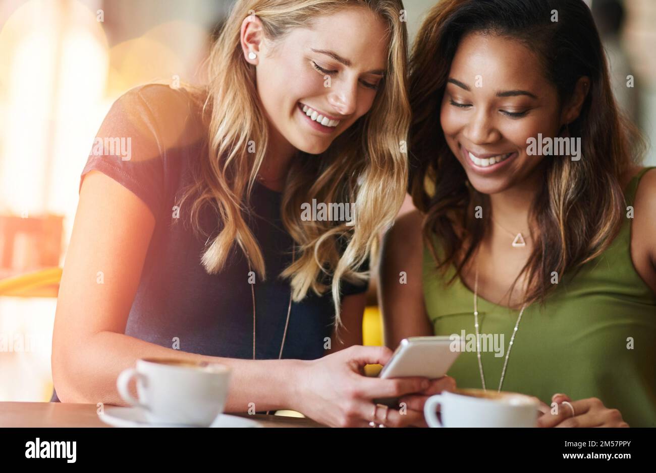 Lets invite all the girls here. girlfriends sharing something on a cellphone while sitting in a cafe. Stock Photo