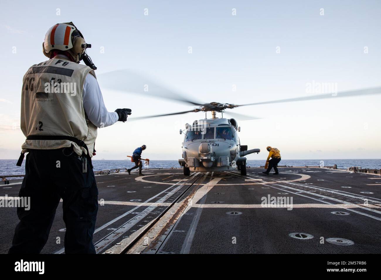 221222-N-YV347-1092 PACIFIC OCEAN (Dec. 22, 2022) U.S. Navy Boatswain’s Mate 2nd Class Joel Dominic Lazo, from San Jose, Calif., signals to the pilot of an MH-60R Sea Hawk helicopter assigned to the 'Battlecats' of Helicopter Maritime Strike Squadron (HSM) 73 on the flight deck of the Ticonderoga-class guided-missile cruiser USS Bunker Hill (CG 52). Bunker Hill, part of the Nimitz Carrier Strike Group, is currently underway in 7th Fleet conducting routine operations. 7th Fleet is the U.S. Navy ‘s largest forward-deployed numbered fleet, and routinely interacts and operates with 35 maritime nat Stock Photo
