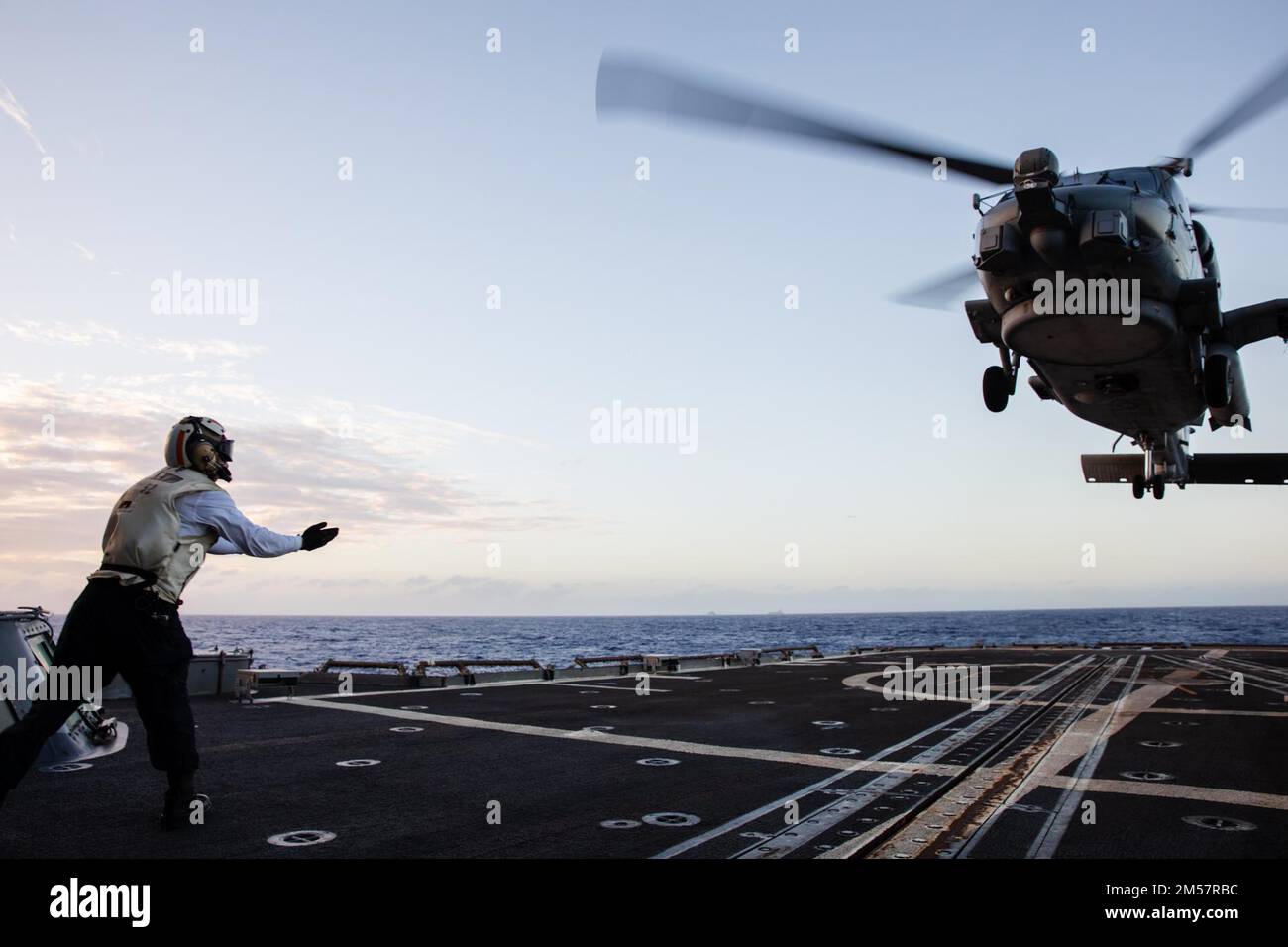 221222-N-YV347-1145 PACIFIC OCEAN (Dec. 22, 2022) U.S. Navy Boatswain’s Mate 2nd Class Joel Dominic Lazo, from San Jose, Calif., uses hand signals to guide the pilot of an MH-60R Sea Hawk helicopter assigned to the 'Battlecats' of Helicopter Maritime Strike Squadron (HSM) 73 on the flight deck of the Ticonderoga-class guided-missile cruiser USS Bunker Hill (CG 52). Bunker Hill, part of the Nimitz Carrier Strike Group, is currently underway in 7th Fleet conducting routine operations. 7th Fleet is the U.S. Navy ‘s largest forward-deployed numbered fleet, and routinely interacts and operates with Stock Photo