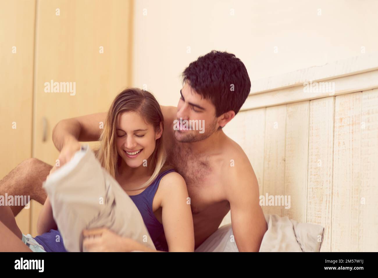 You never know when a pillow fight will break out. a happy young man initiating a pillow fight with his girlfriend in bed. Stock Photo