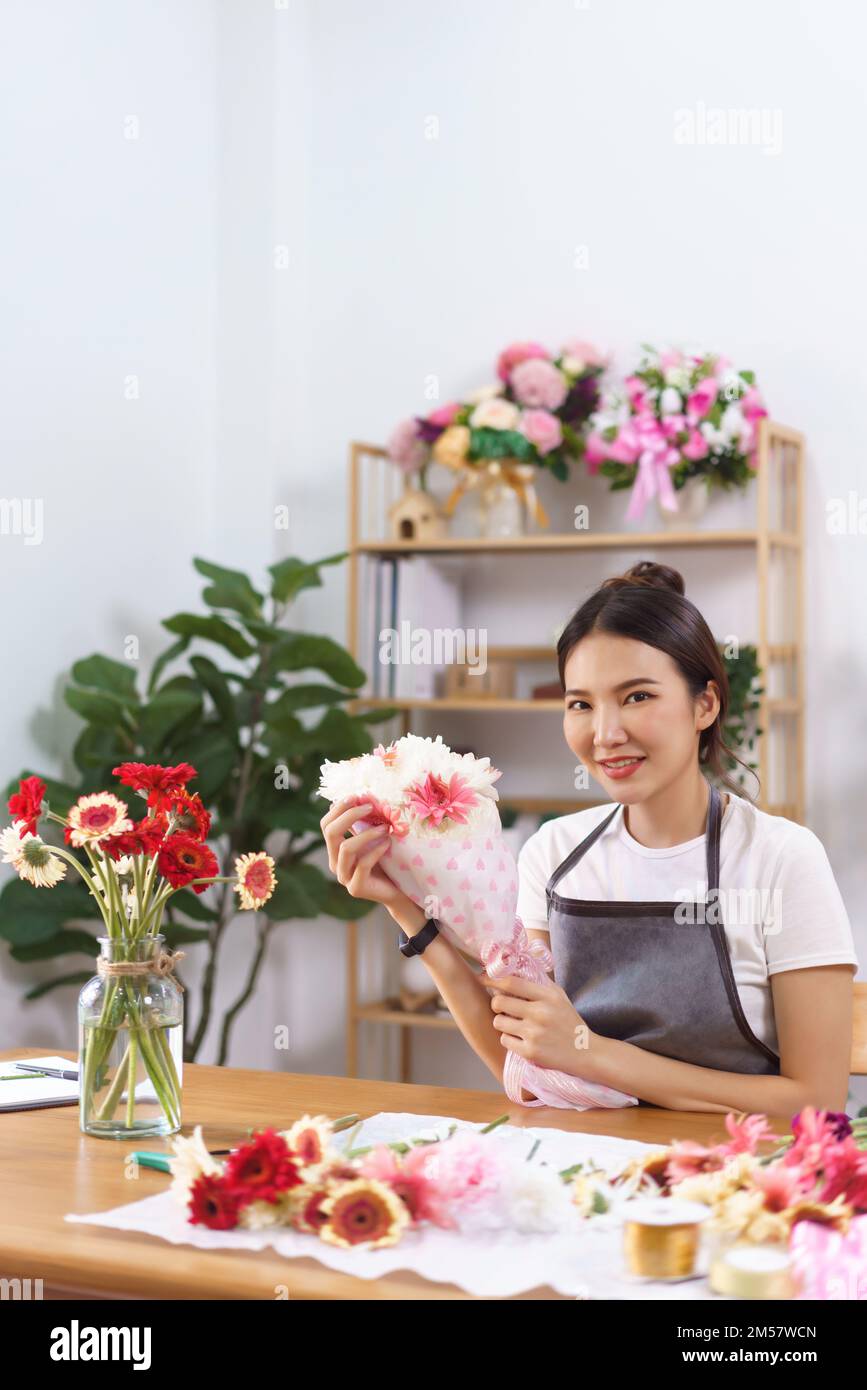 Flower shop concept, Female florist smile and holds colorful flower bouquet with paper and ribbon. Stock Photo