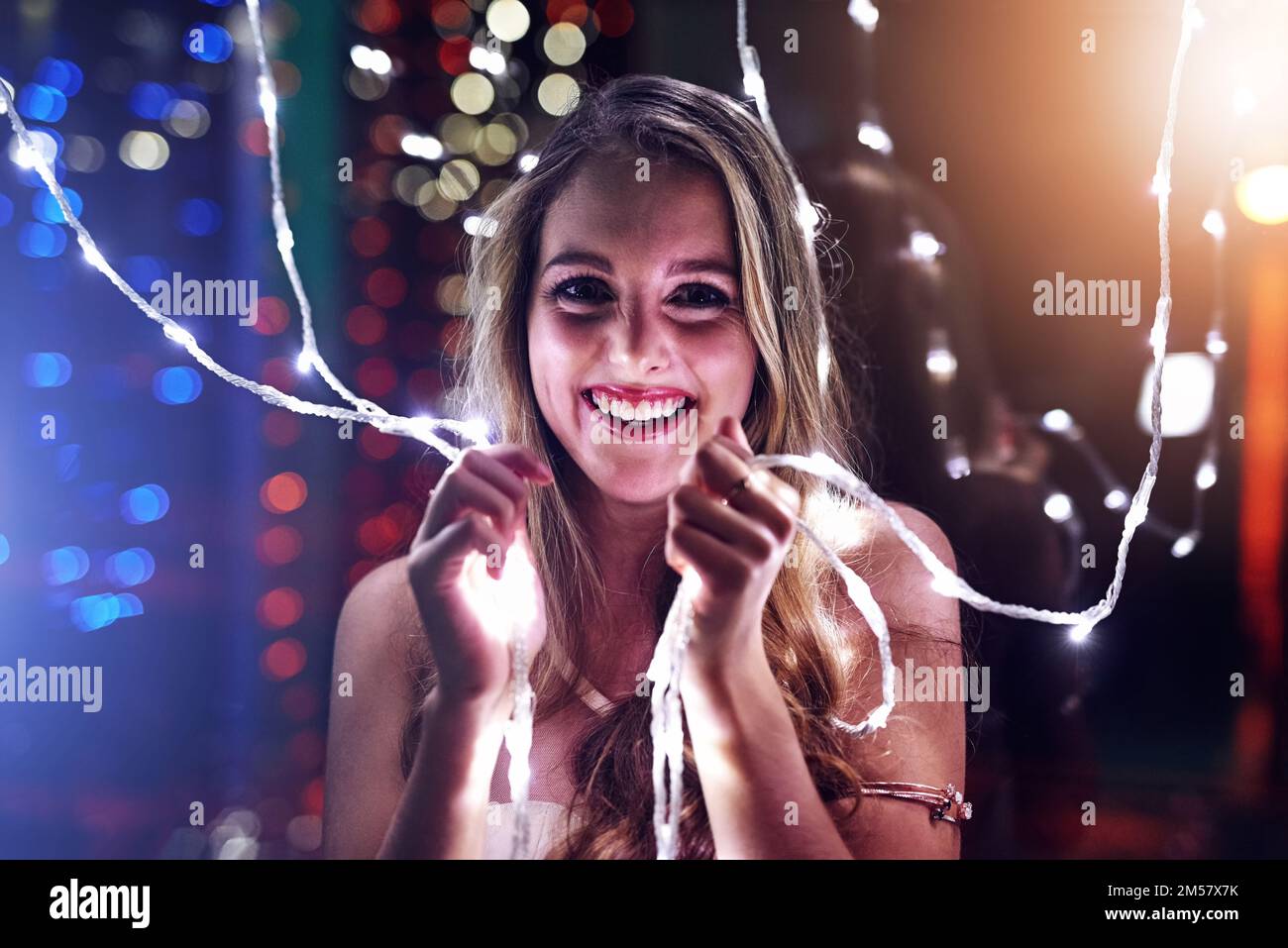 Lighting up the night. Portrait of a happy young woman playing with string lights in a night club. Stock Photo