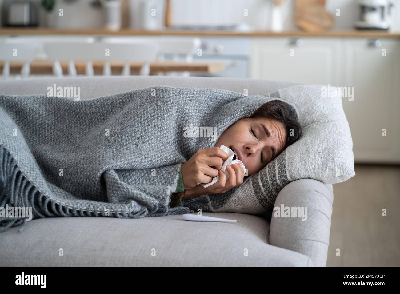 Sick woman with weakened immunity sneezing in tissue while lying under