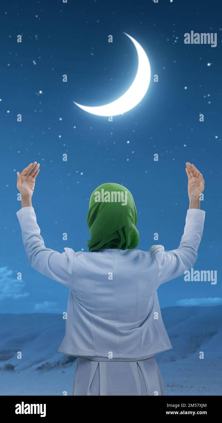 The rear view of a Muslim woman in a veil raising a hand and praying in ...