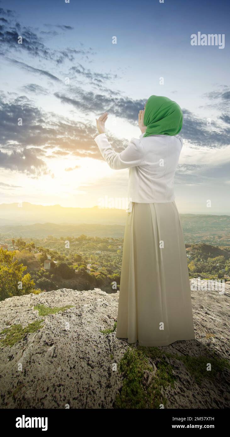 The rear view of a Muslim woman in a veil raising a hand and praying in ...
