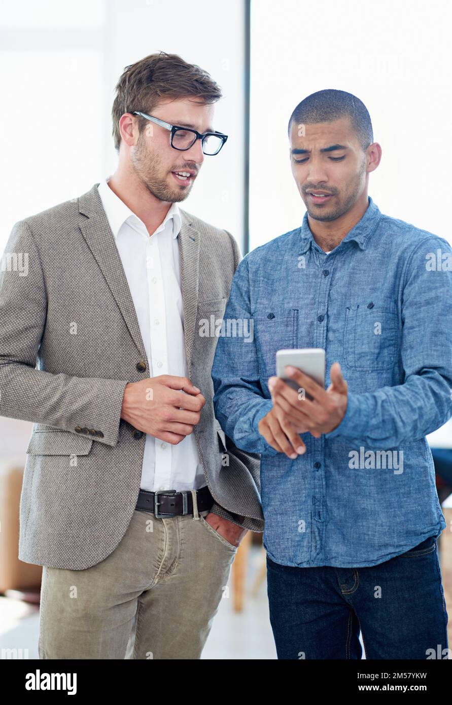 Developing great new apps. two colleagues discussing something on a cellphone. Stock Photo