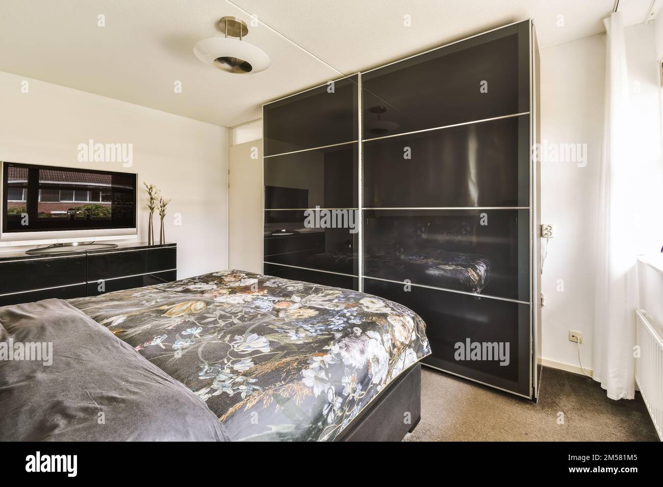 a bedroom with a large bed and black wardrobes on the wall, in front of a  flat screen tv Stock Photo - Alamy, image size:1300x956