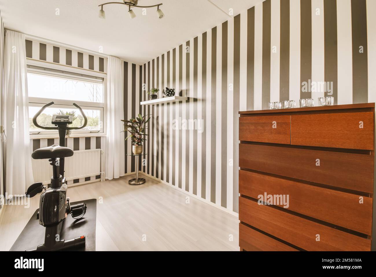 a living room with black and white striped wallpapers on the walls, an exercise bike in the corner Stock Photo