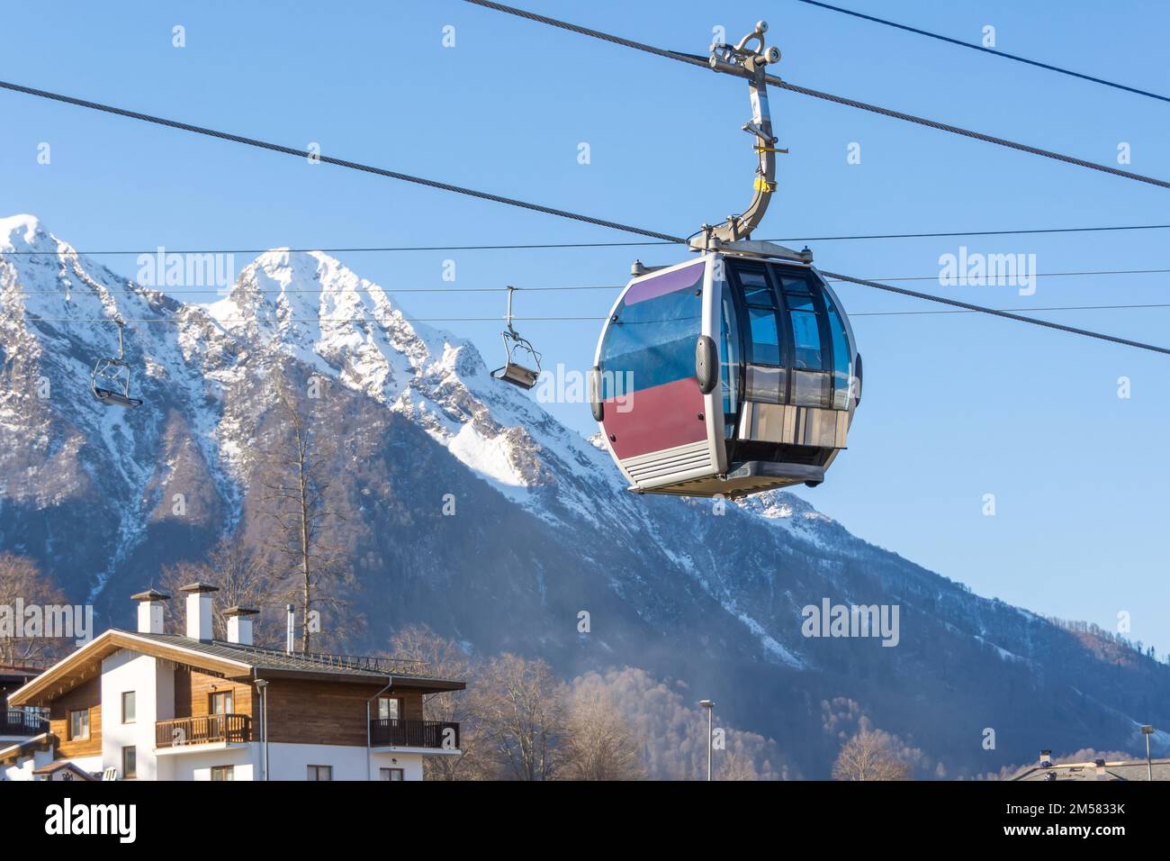 Cable car on the slopes of a ski resort with houses and a snowy peak in ...