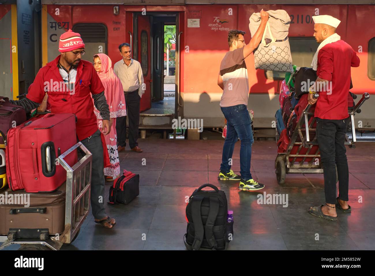 Passengers and porters on a platform of  Chhatrapati Shivaji Maharaj Terminus in Mumbai, India, a newly arrived train in the background Stock Photo