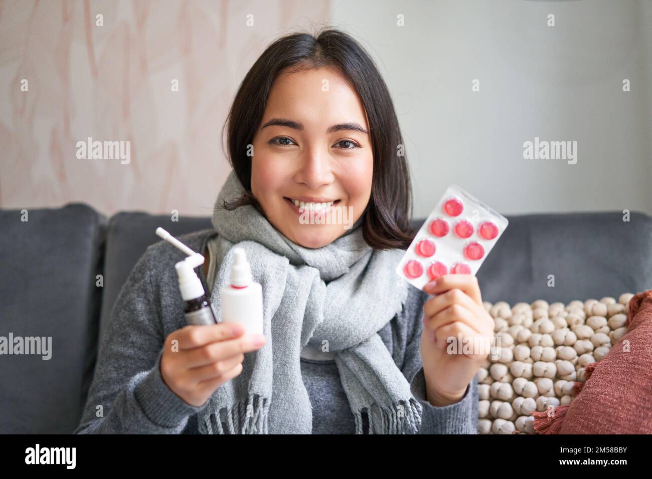 Portrait of happy smiling asian girl showing medication, sore throat spray and drugs from flu or