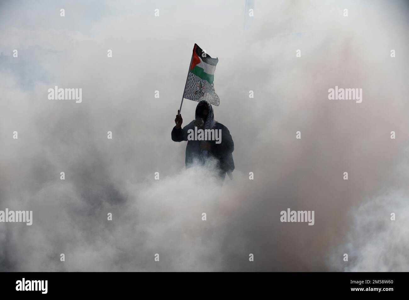 A Palestinian protestor stands amid tear gas, as Palestinians clash with Israeli forces during a protest against what organizers say are Israel's measures of keeping bodies of dead prisoners, near Qalandia in the Israeli-occupied West Bank December 27, 2022. REUTERS/Mohamad Torokman      TPX IMAGES OF THE DAY Stock Photo