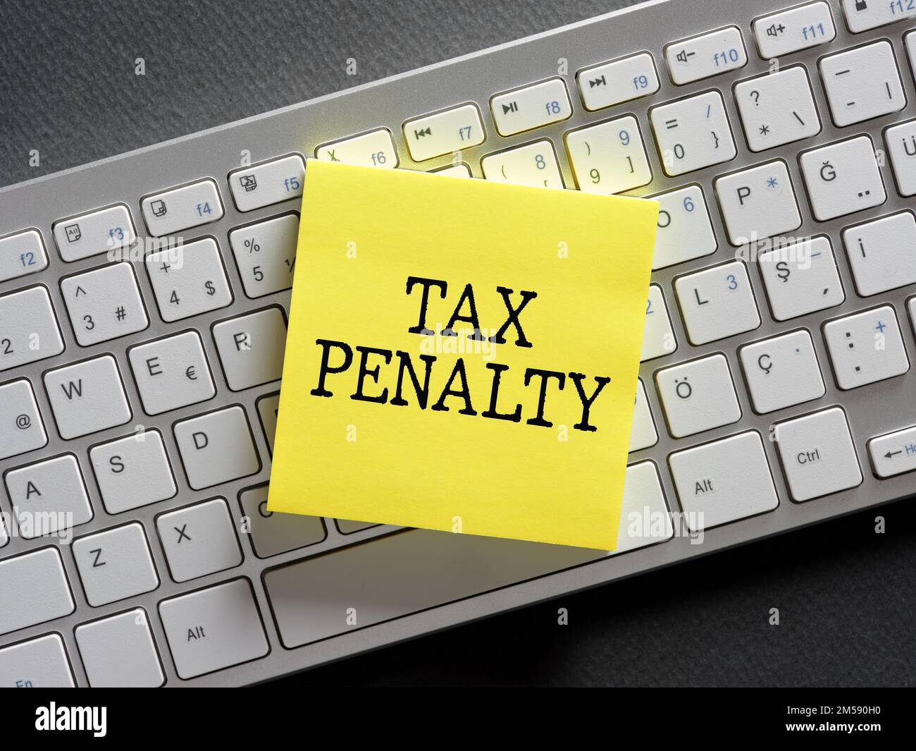 The word tax penalty written on a sticky note paper on computer keyboard. Stock Photo